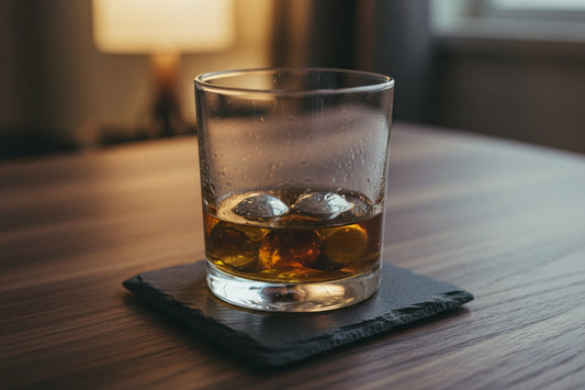 Tumbler of whisky with polished steel cooling cubes on a slate coaster