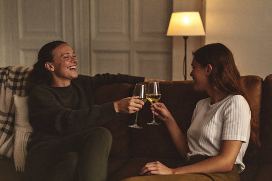 Two women toasting with white wine on a sofa